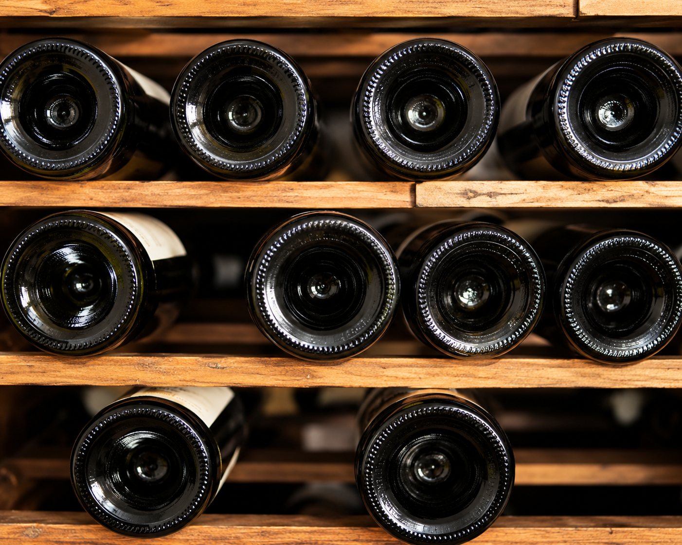 Des bouteilles de vin sont rangées horizontalement sur des étagères en bois, vues par le fond.