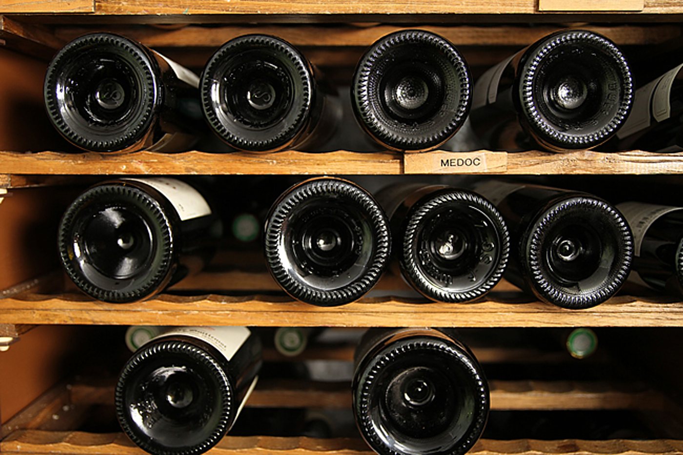 Des fonds de bouteilles de vin sont alignés sur des étagères en bois, avec une étiquette indiquant Médoc.