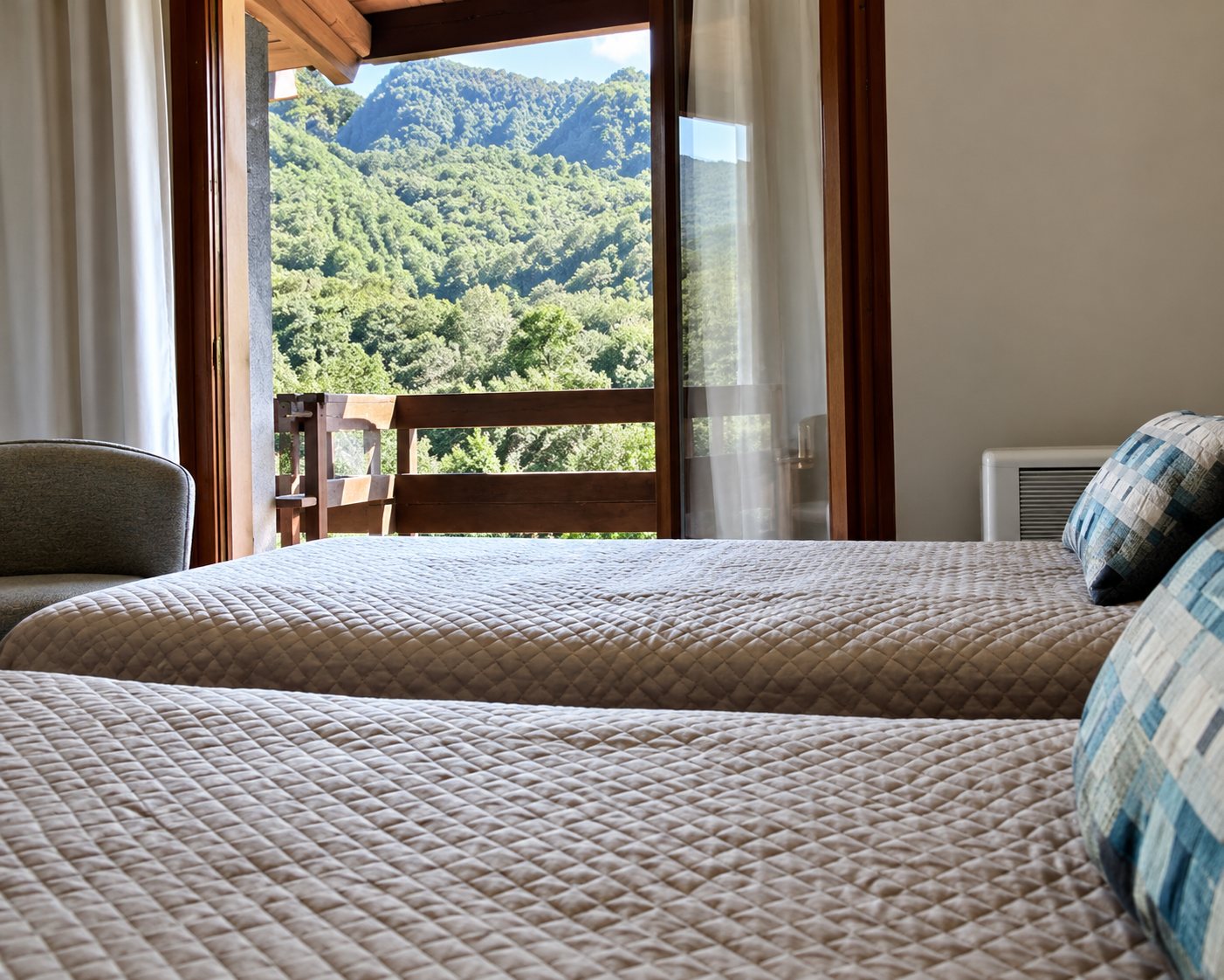 Une chambre lumineuse avec deux lits et une grande fenêtre ouverte sur un paysage de verdure.