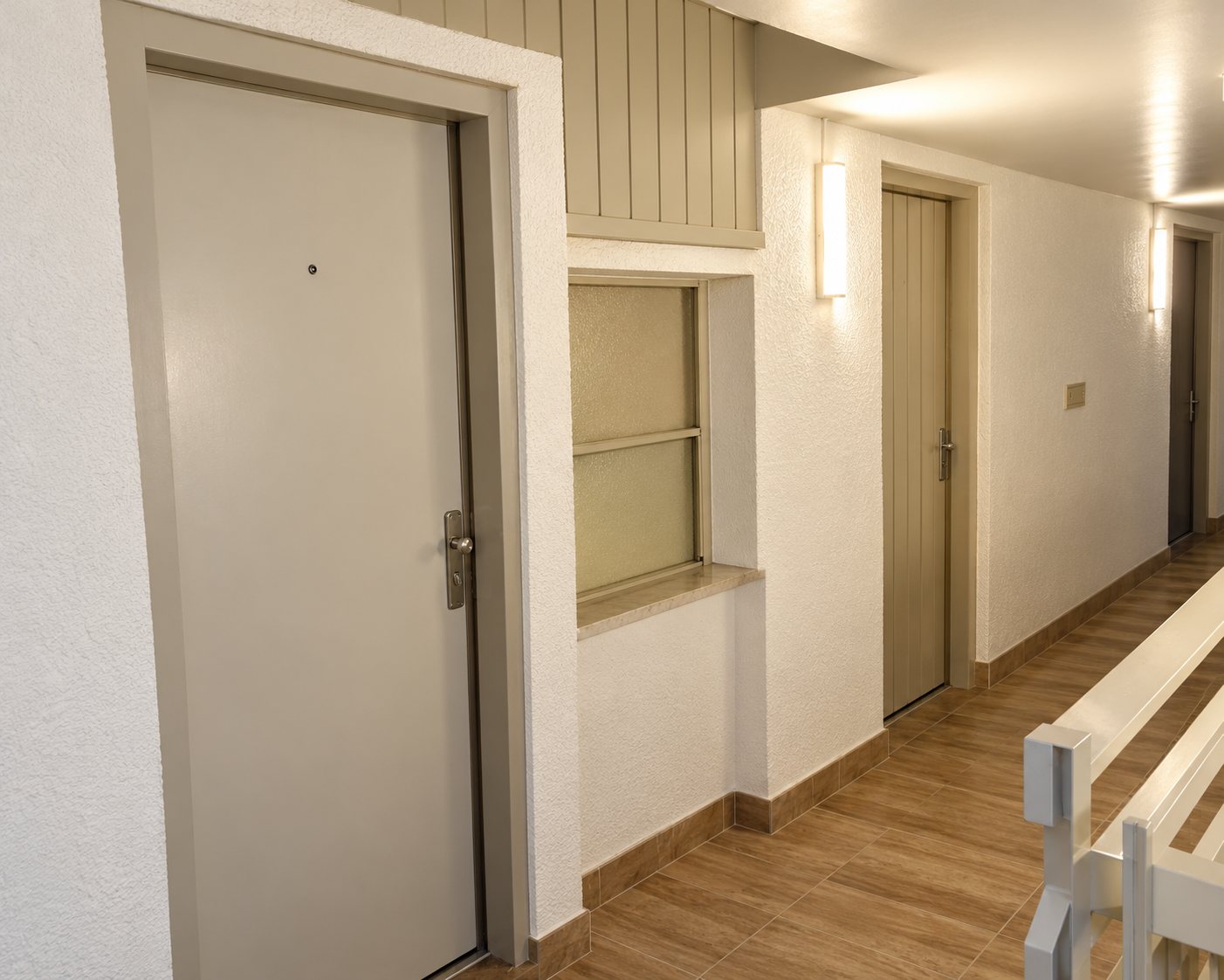 Un couloir lumineux aux murs clairs, avec plusieurs portes blanches et un sol en parquet au premier plan.