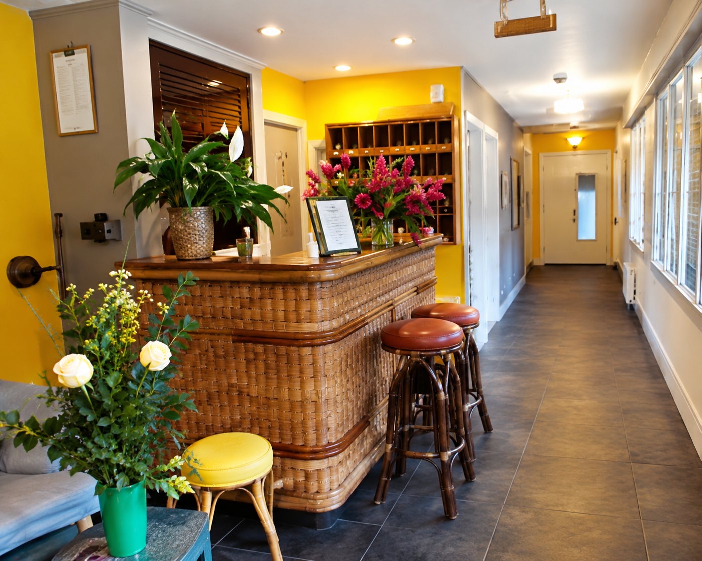 Vue de l'intérieur d'un petit commerce avec un comptoir en bois orné de plantes, un tabouret jaune au premier plan et un couloir lumineux au fond.