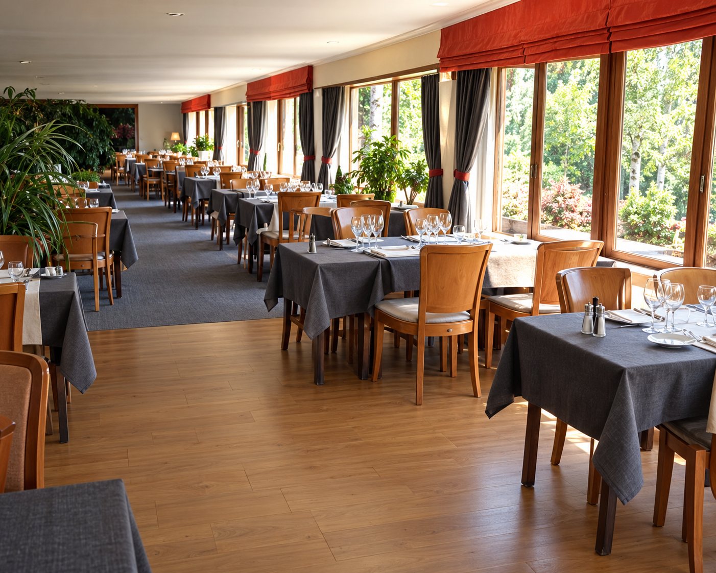 Intérieur d'une salle de restaurant avec des tables dressées alignées le long de grandes fenêtres laissant entrer la lumière.