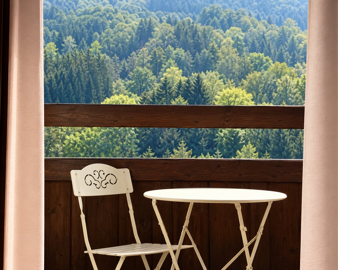Une petite table ronde blanche et une chaise sont installées sur un balcon avec vue sur des collines couvertes d'arbres.